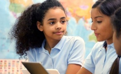 School girls sit at desk looking at iPad.